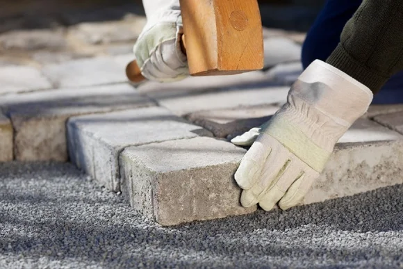 Person verlegt Pflastersteine mit Hammer